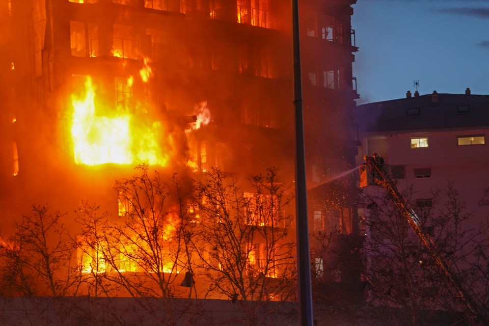 Firefighters spray water on the housing block as it burns