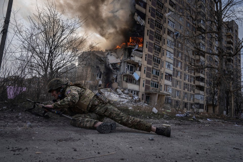 A Ukrainian soldier in front of a burning building that was hit by Russian airstrikes in Avdiivka