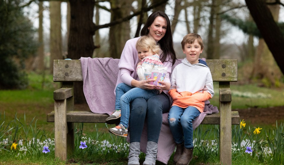 a woman sits on a wooden bench with two children