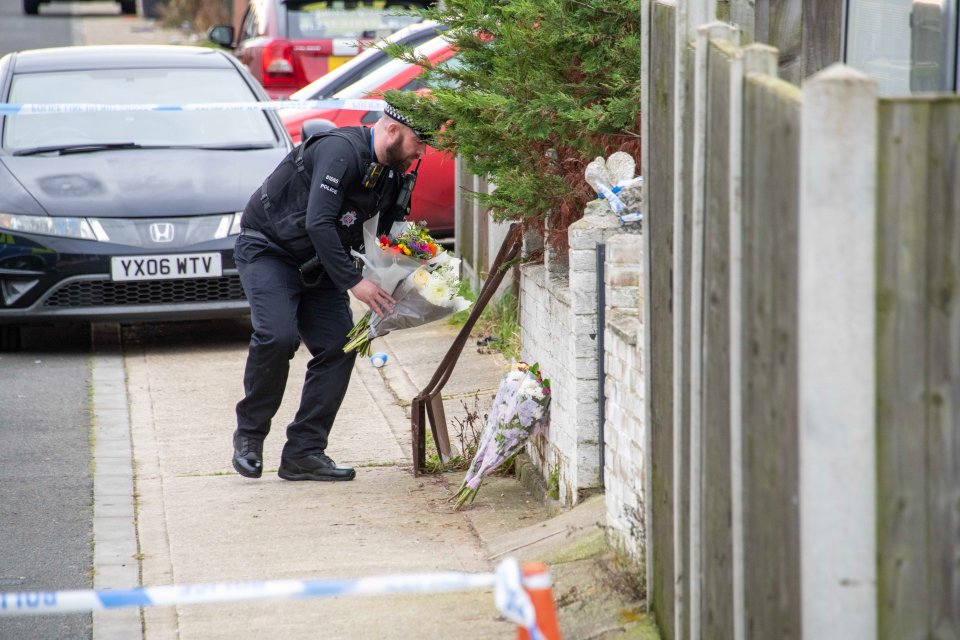 An officer places a floral tribute outside the address