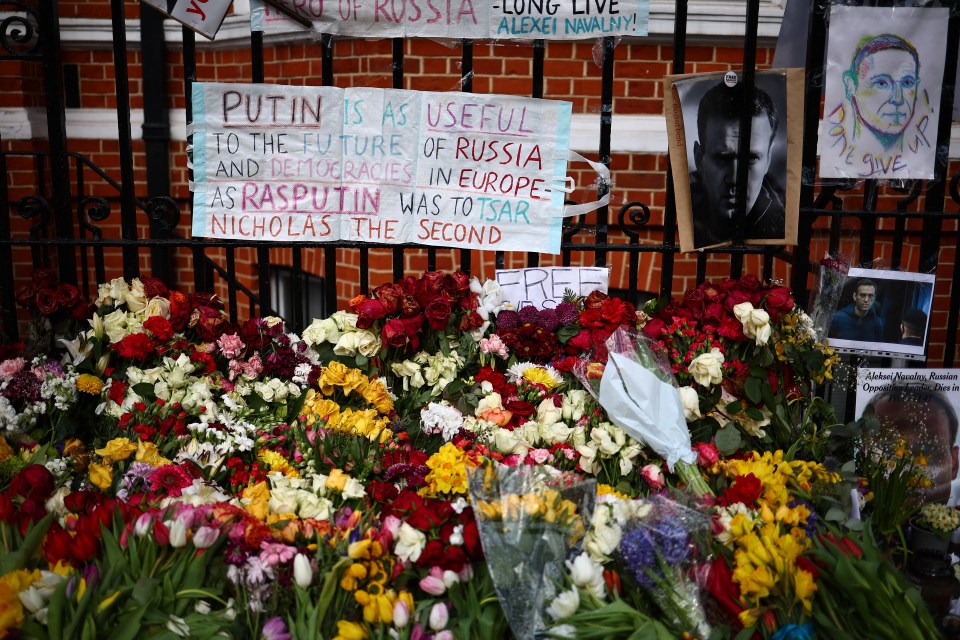 Flowers are seen placed beside photographs and placards opposite the Russian Embassy in London