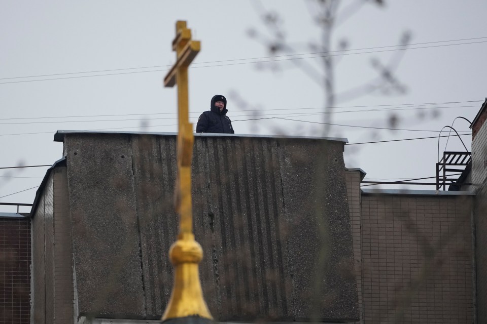 A police officer stands guard on the roof of an apartment building near the church