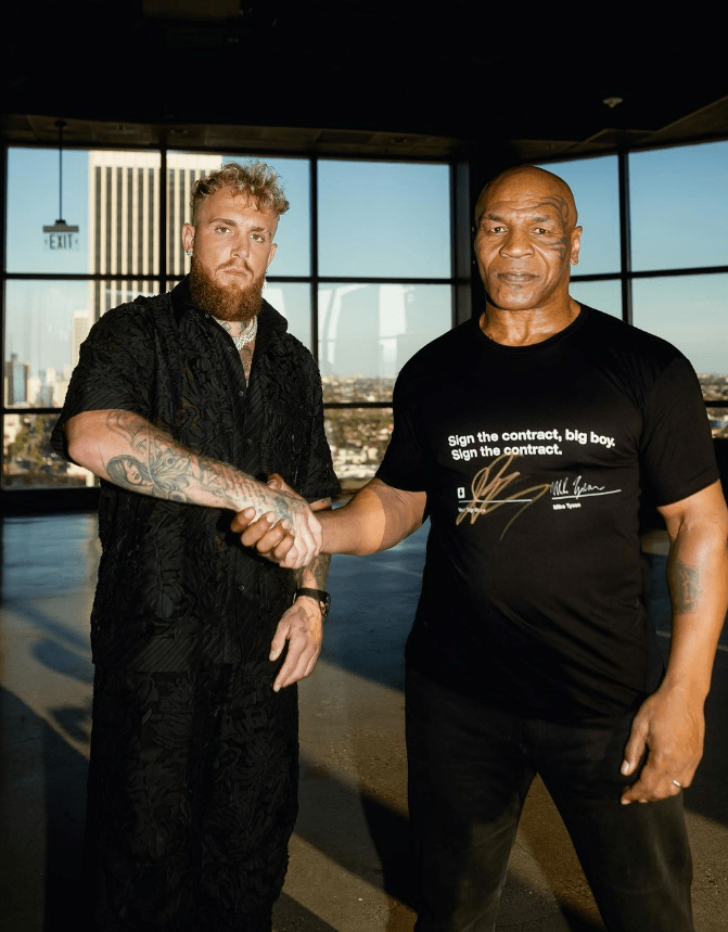 two men shaking hands with one wearing a shirt that says " sign the contract big boy sign the contract "