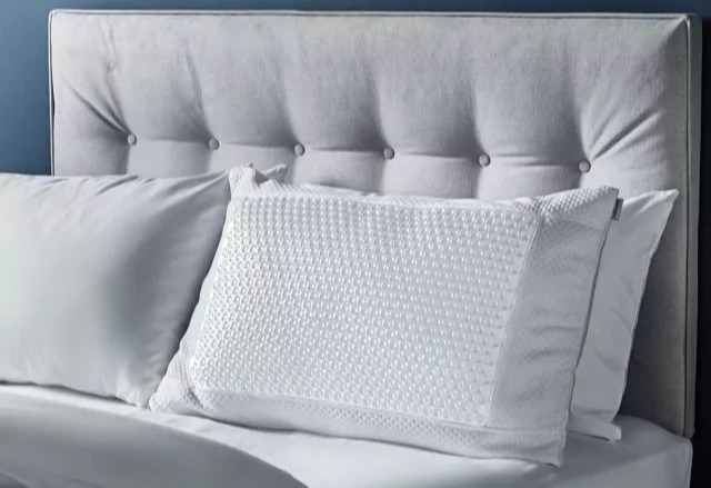 Grey upholstered headboard with white pillows on a bed.