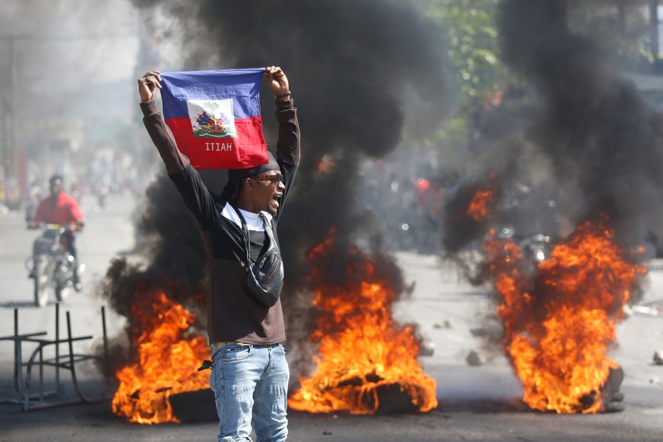 A thug holds up a Haitian flag during protests demanding the resignation of Prime Minister Ariel Henry