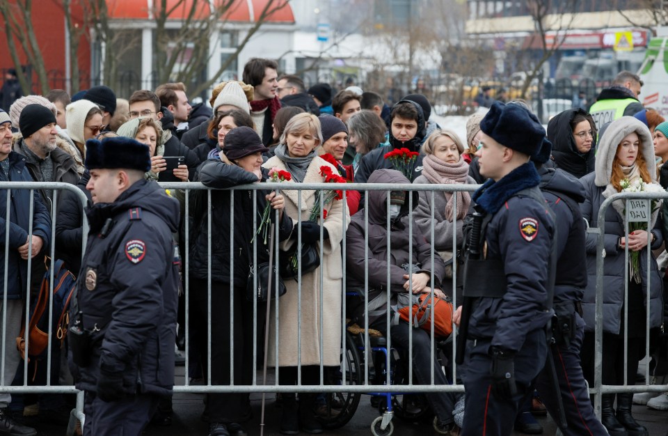 Police officers walk past crowds gathered outside the church