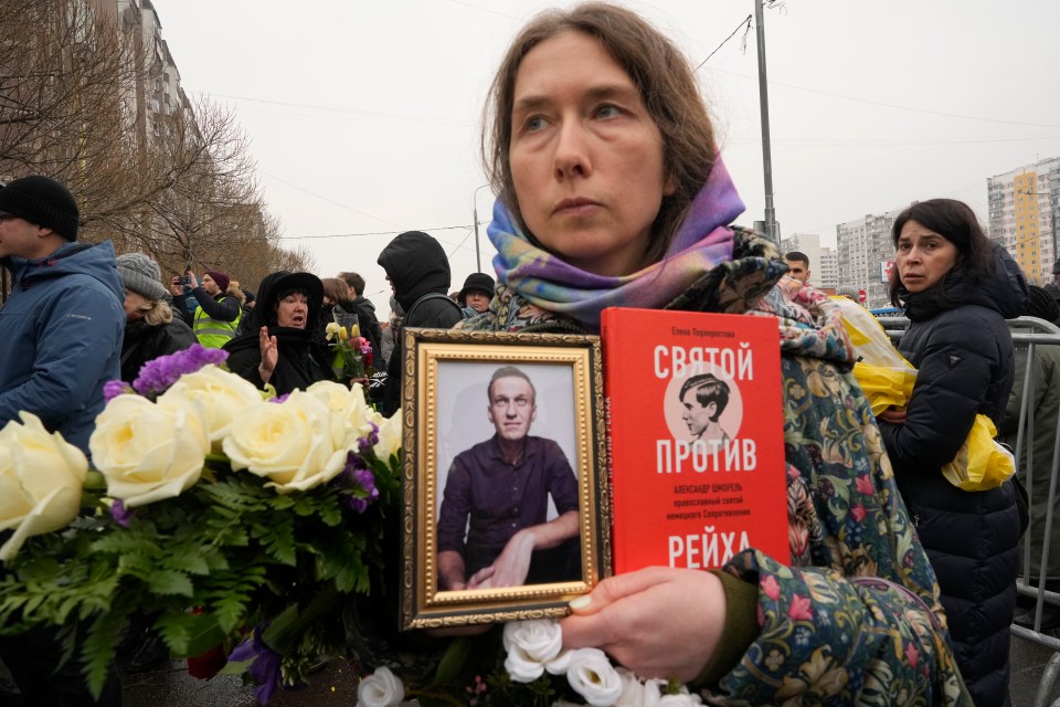 A woman holds a portrait of Alexei Navalny and a book titled 'A saint against the Reich'