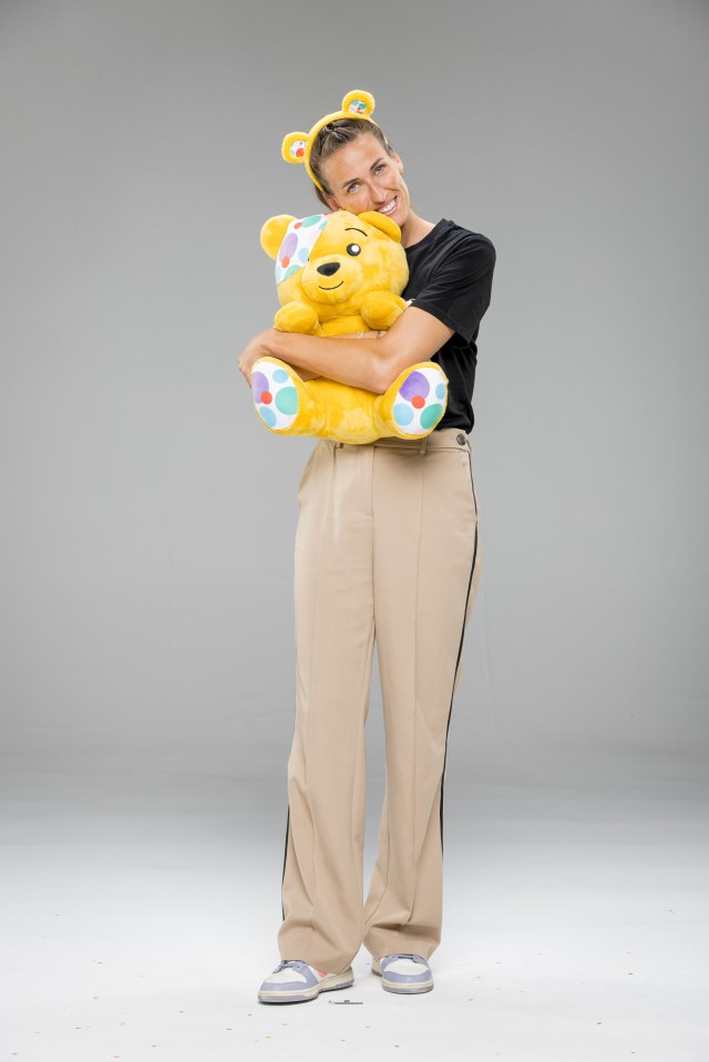 a woman in a black shirt and tan pants is holding a yellow teddy bear