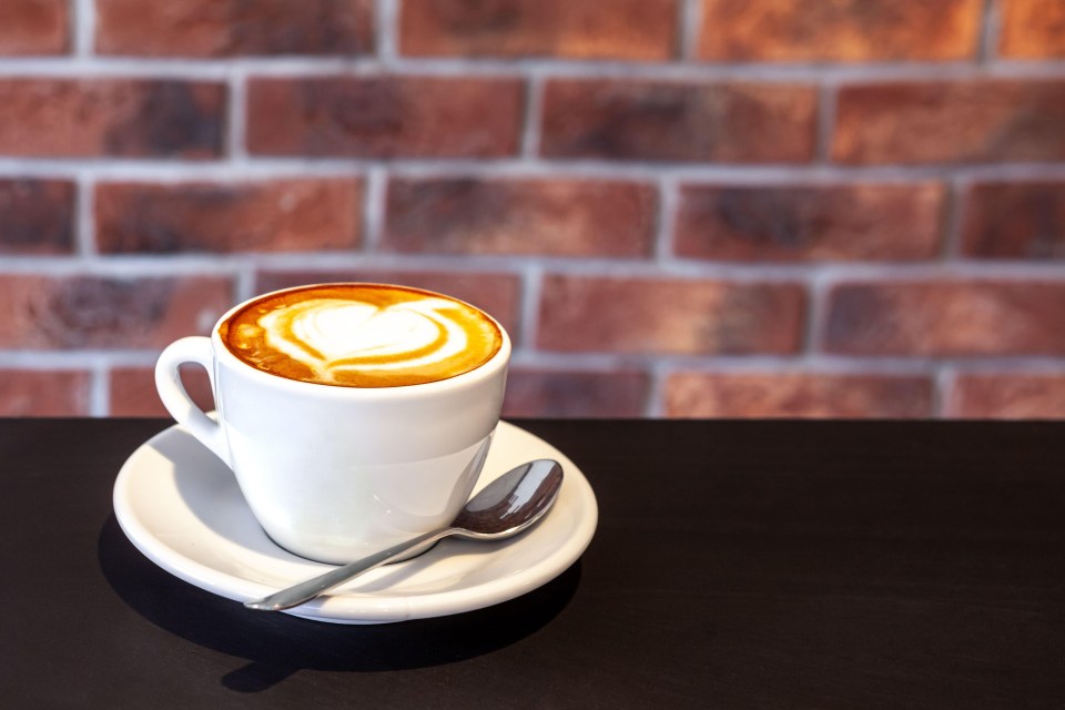 a cup of cappuccino on a saucer with a spoon in front of a brick wall