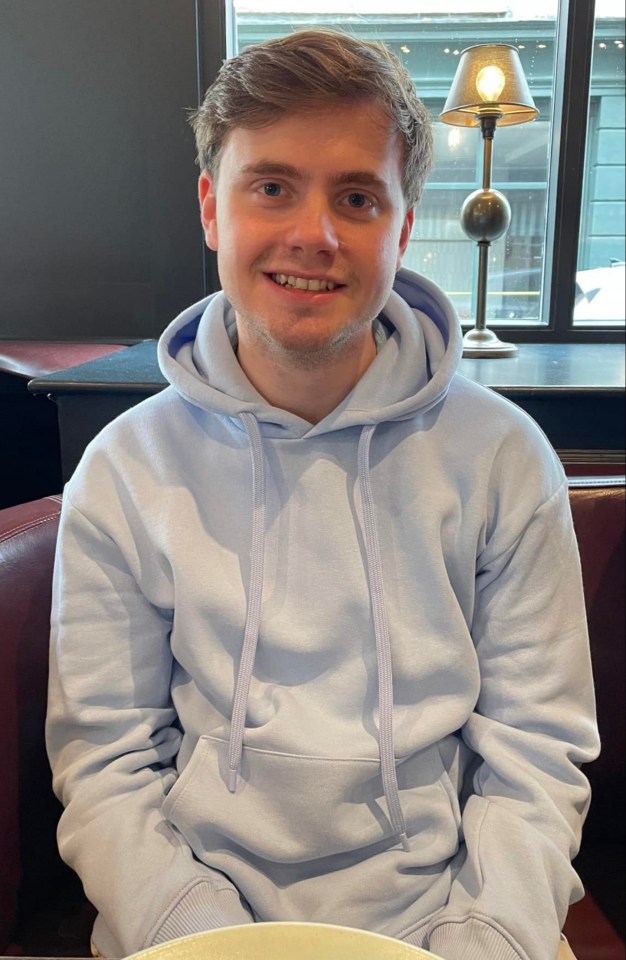 a young man wearing a light blue hoodie smiles for the camera