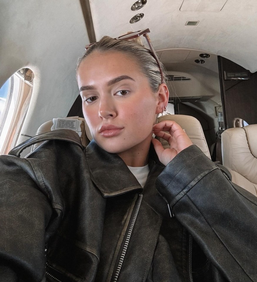 a woman in a leather jacket is sitting on an airplane