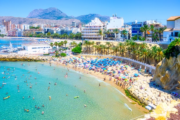 People swimming, resting, and sunbathing on a beautiful beach in Benidorm, Spain.