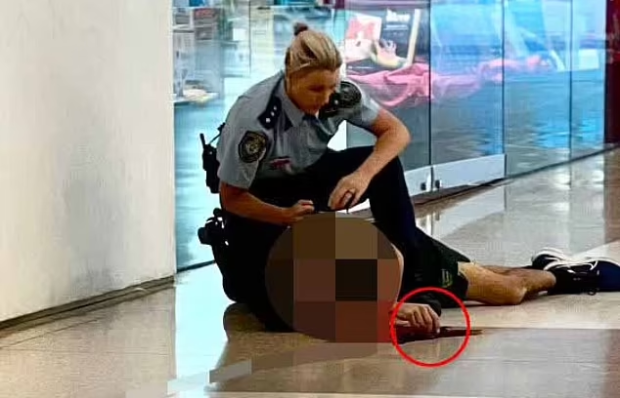 A police officer crouches over the body of the attacker in Sydney after he stabbed at least six shoppers