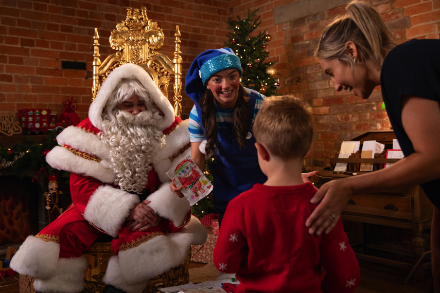 a woman in a blue hat stands next to a boy in a red sweater and a man in a santa suit