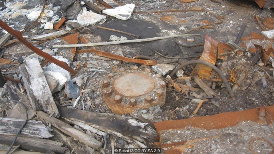 The hole is covered by a heavy-duty maintenance lid secured into place by rusty bolts