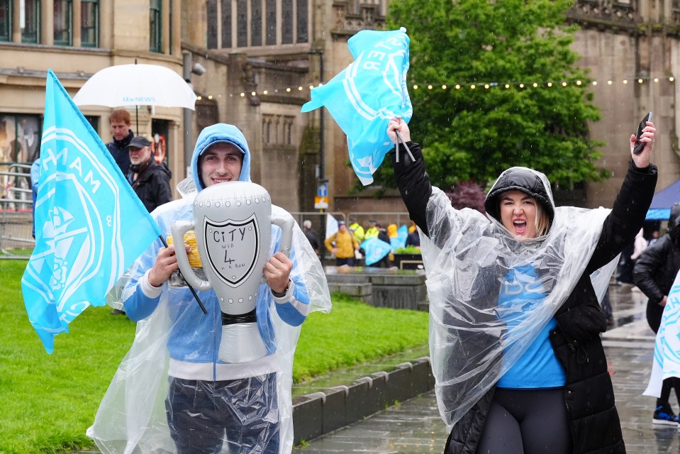 Pals in ponchos hold a mock trophy as they celebrate in the wet