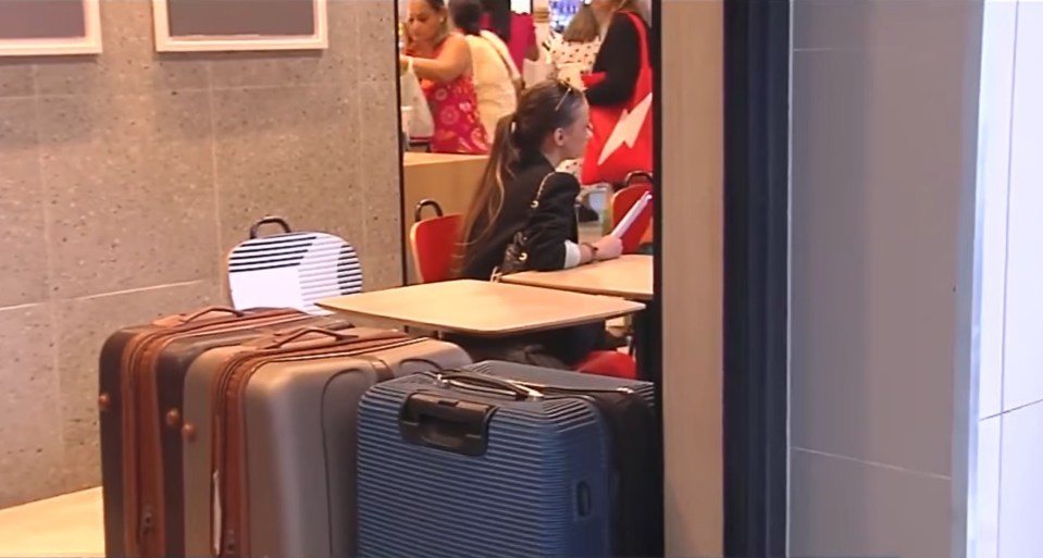 a woman sits at a table with a suitcase that says ' slazenger ' on it