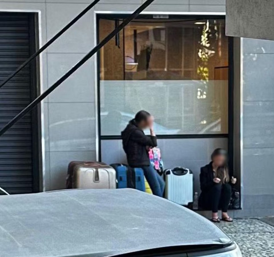 a woman sits in front of a building with luggage