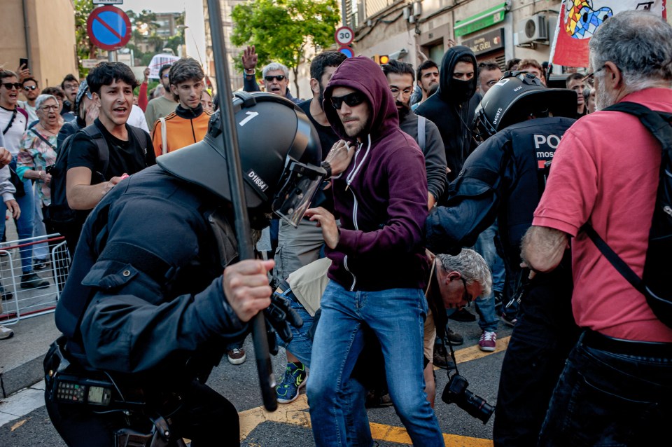 A cop raises a baton at a protester in the Park Guell neighbourhood of Barcelona