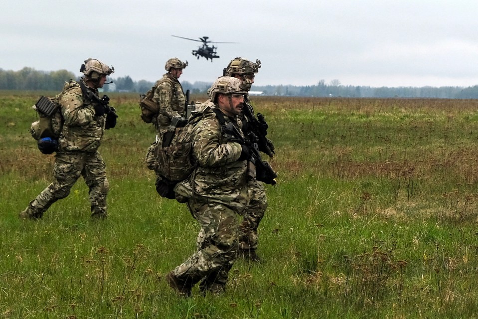 a group of soldiers walking in a field with a helicopter in the background