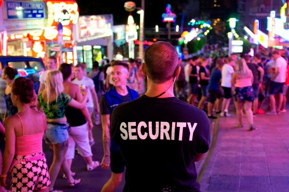 A private security guard observes tourists partying in Punta Ballena street in Majorca