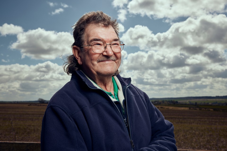 a man wearing glasses and a blue jacket stands in a field