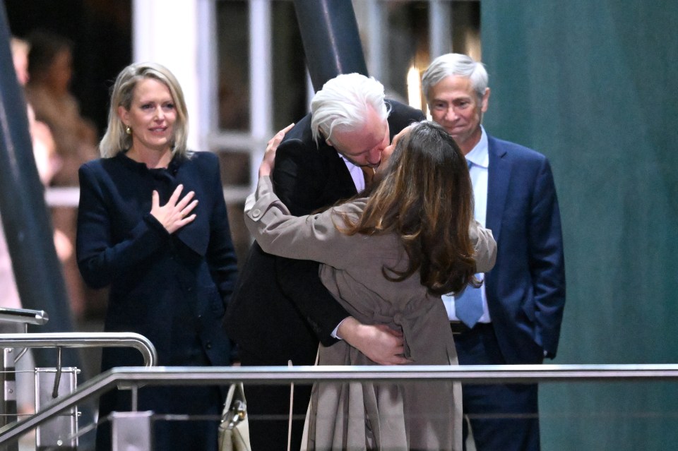 a man in a suit kisses a woman in a trench coat