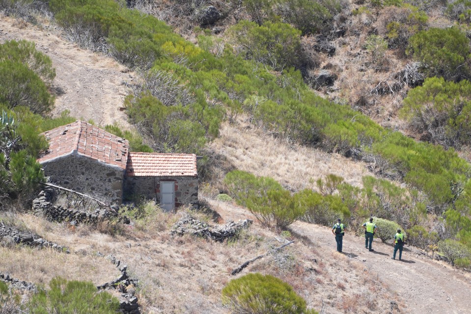 a group of people walking on a dirt path near a stone building