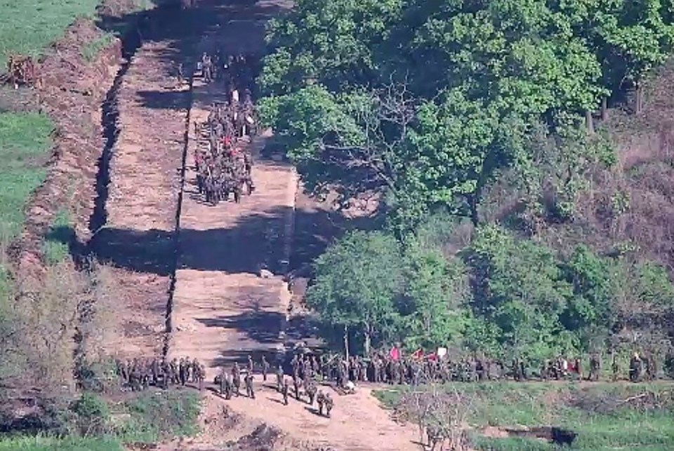 a large group of people are walking down a dirt road