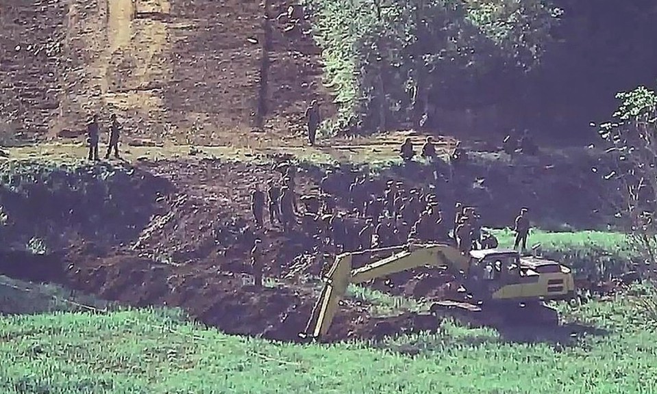 a group of people are standing in a field with a yellow excavator in the foreground .