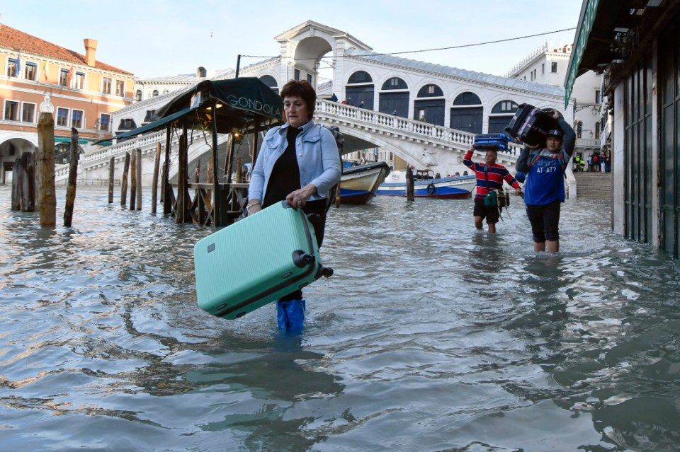 People carry their luggage as they wade through water following extreme flooding in Venice in 2019