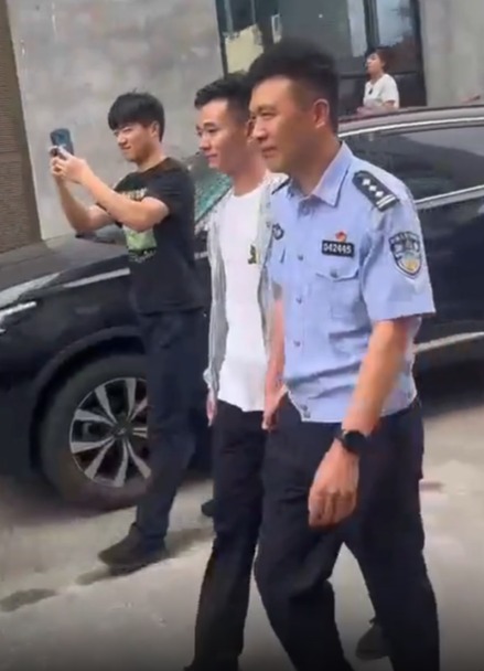 Zhang is walked by a policeman to his family