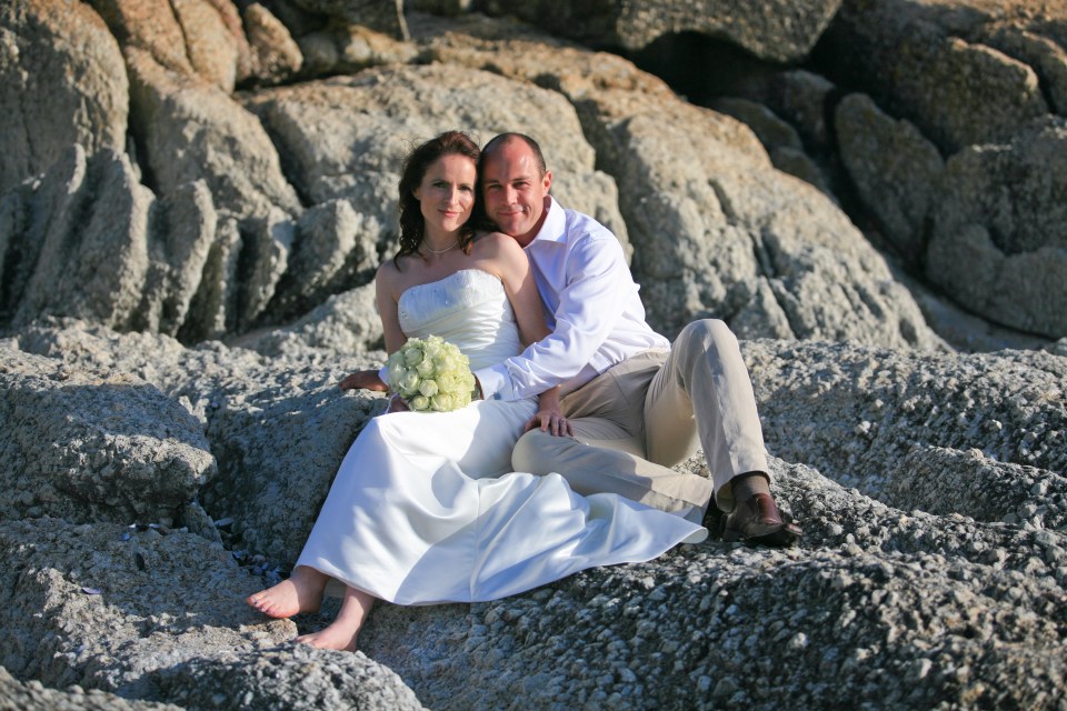 a bride and groom pose for a picture on a rocky beach