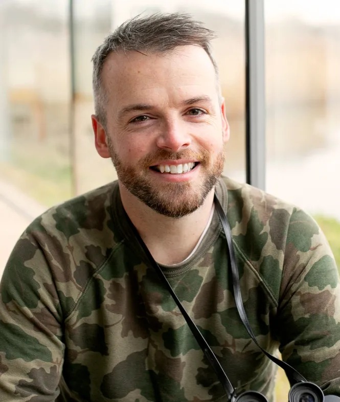 a man wearing a camo sweater is smiling and holding binoculars