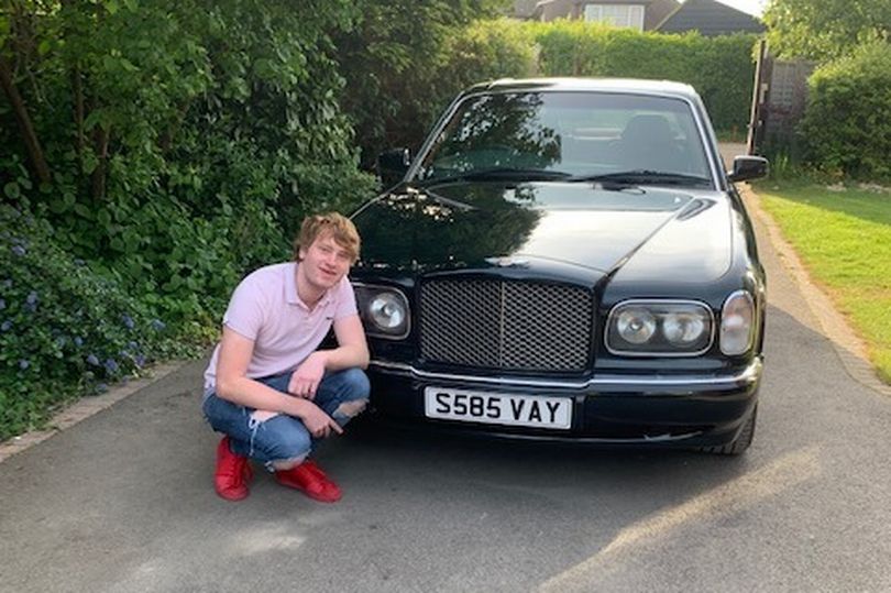 a young man is squatting in front of a black car with a license plate that says s585 vay