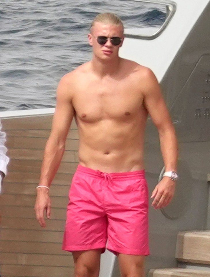 a shirtless man wearing pink swim trunks and sunglasses