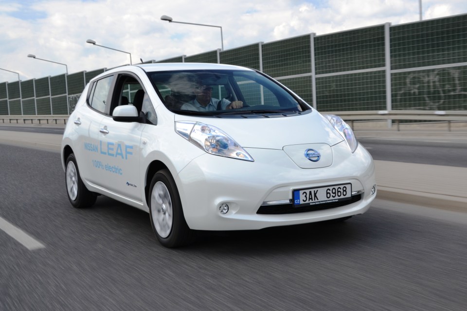 White Nissan Leaf electric car driving on a city street.