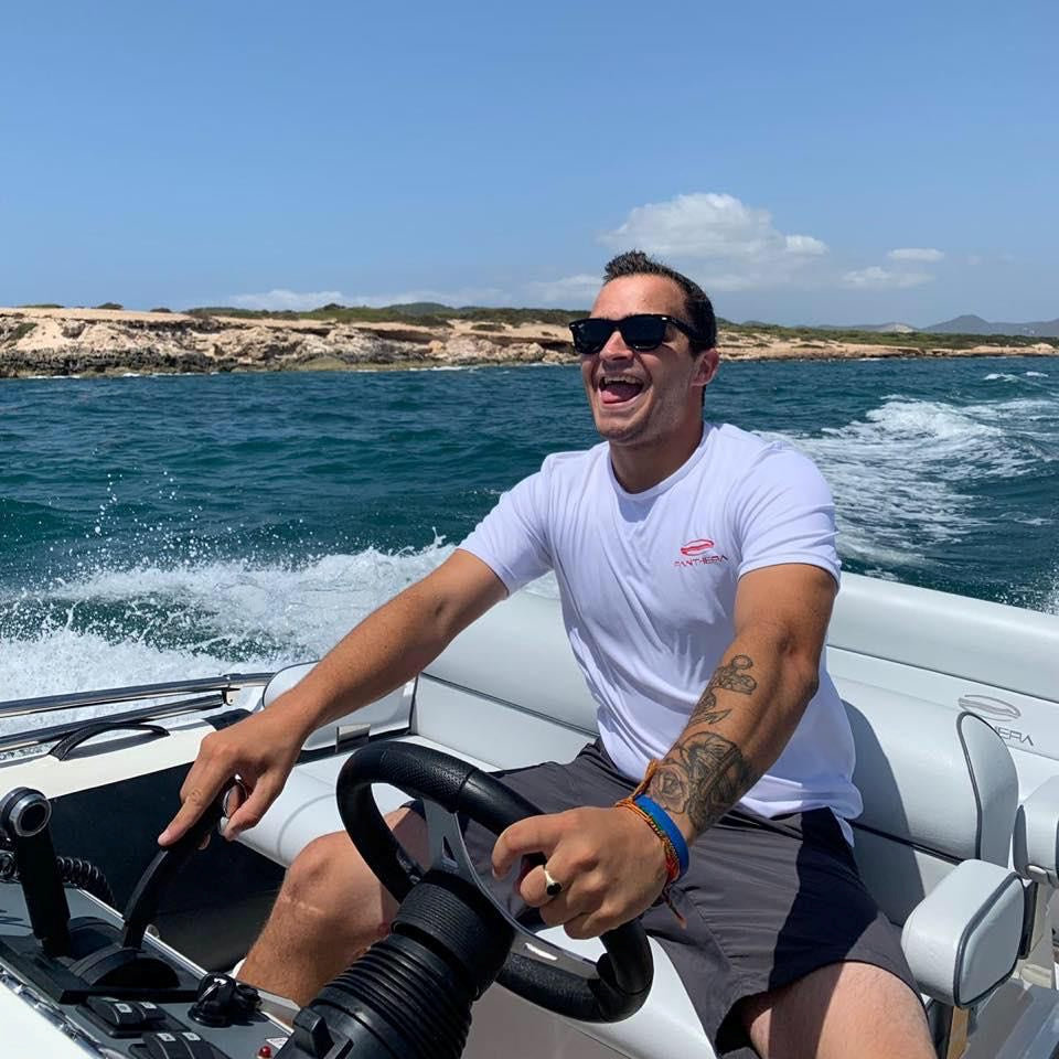 a man wearing a white t-shirt that says sky rider is driving a boat