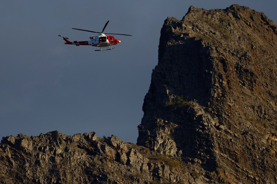 a red and white helicopter is flying over a mountain