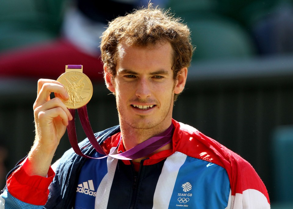 a man wearing an adidas jacket is holding a gold medal