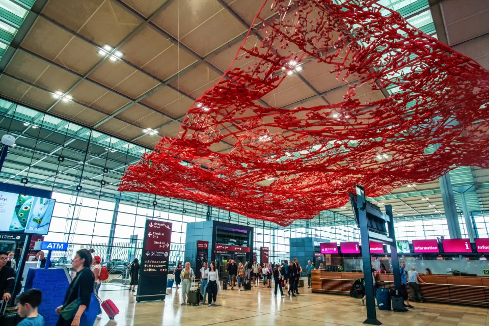 a large red sculpture hangs from the ceiling of an airport