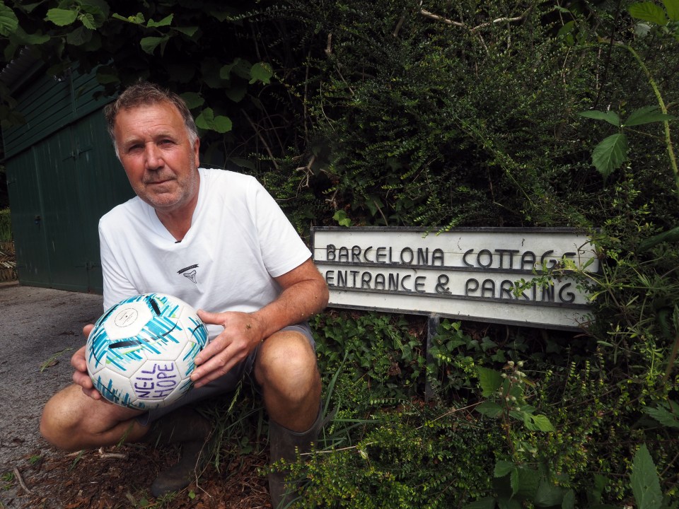 a man holds a ball in front of a sign that says barcelona cottage entrance & parking