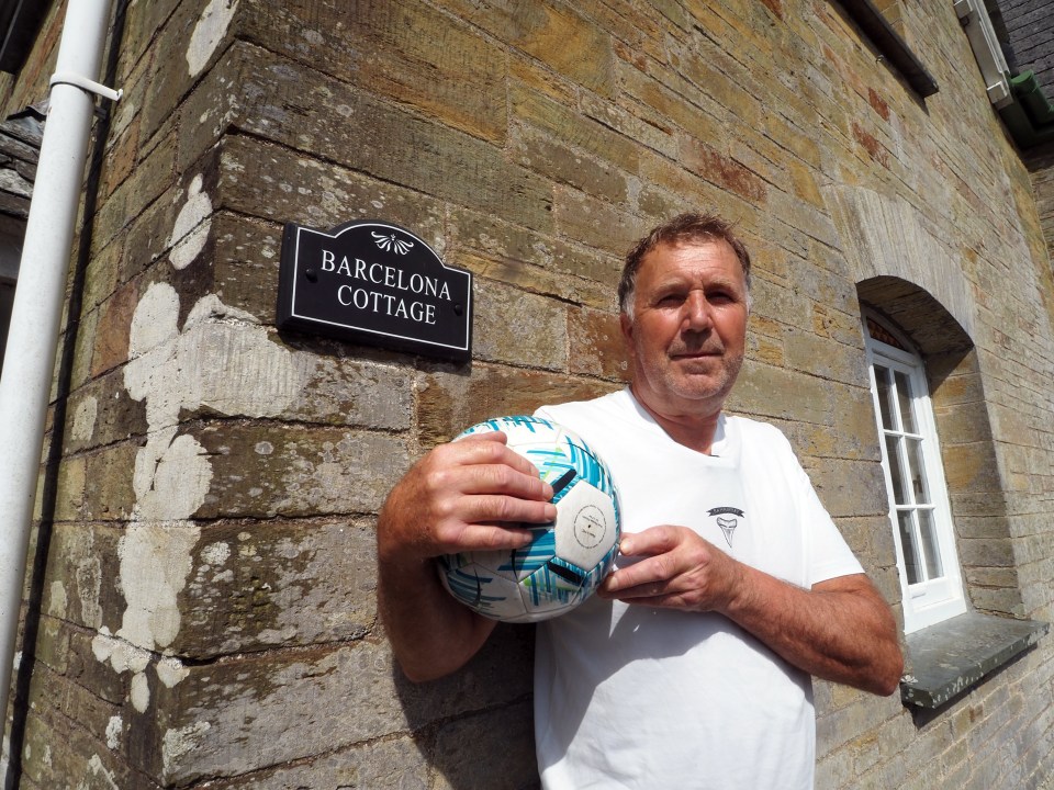 a man holds a soccer ball in front of a sign that says barcelona cottage