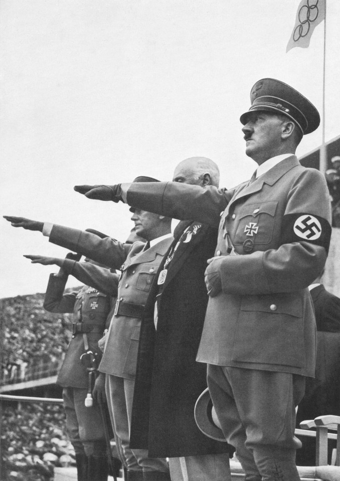 a group of men salute in front of an olympic flag