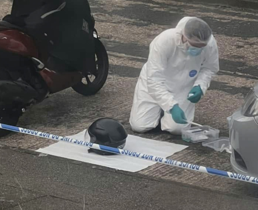 A forensics officer collects evidence next to a moped and helmet