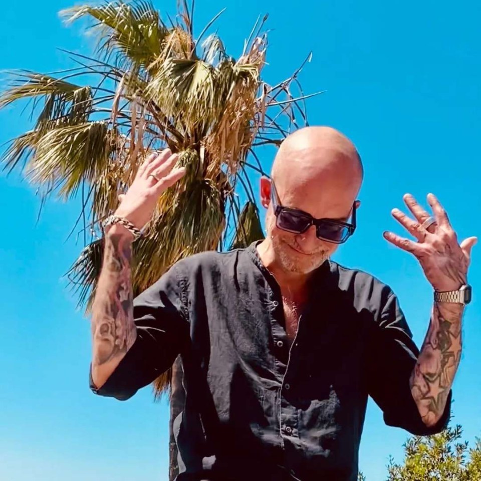 a bald man wearing sunglasses stands in front of a palm tree