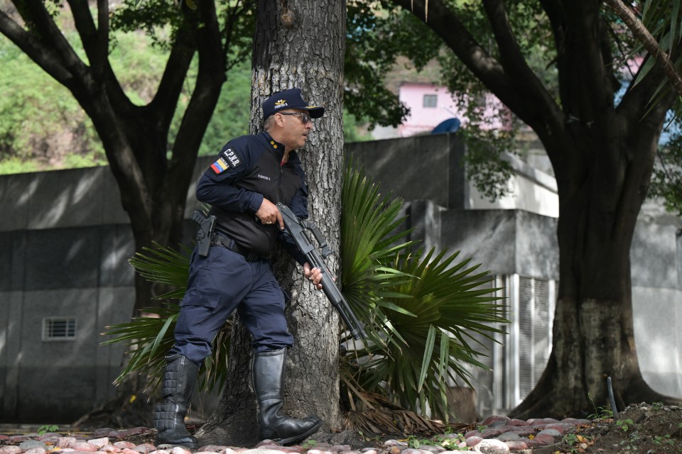 A police officer with a gun takes cover behind a tree