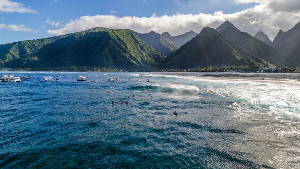 a group of people are swimming in the ocean with mountains in the background