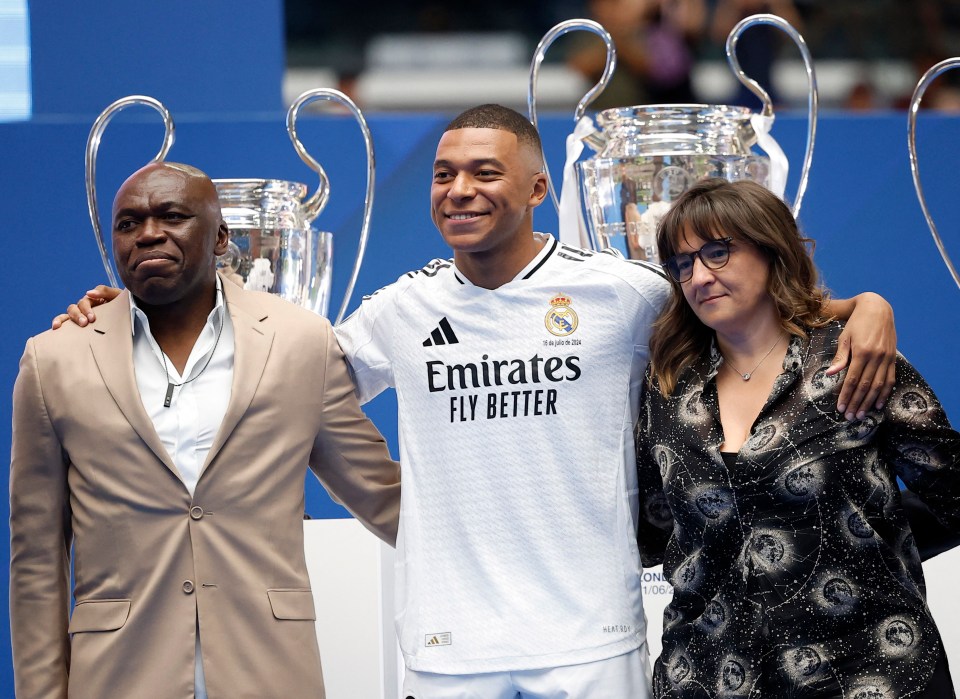 a man wearing an emirates fly better jersey stands with two men and a woman