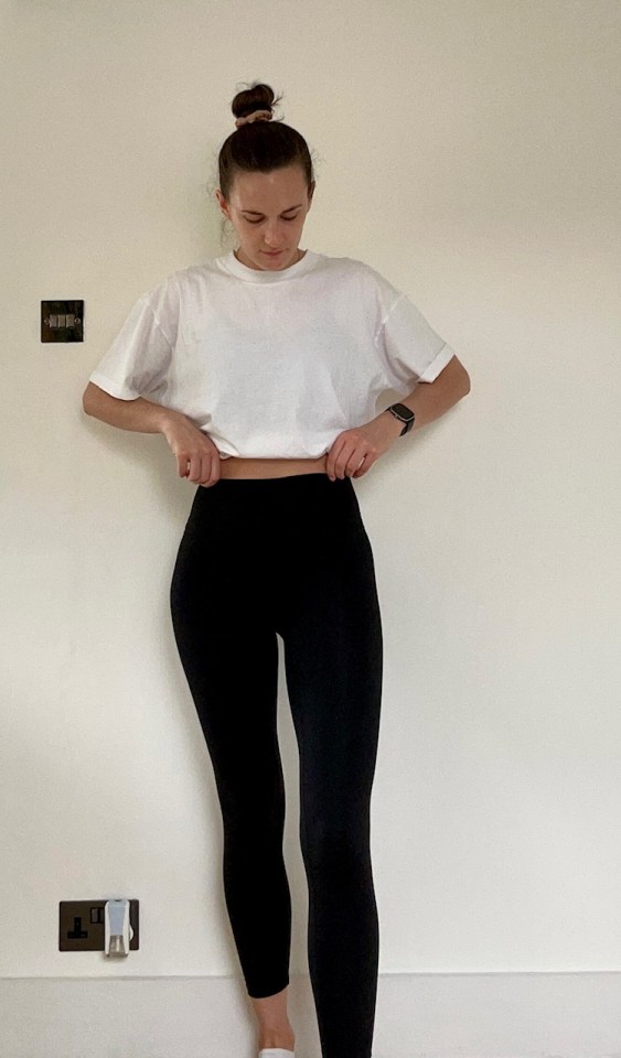 a woman wearing a white t-shirt and black leggings is standing in front of a white wall